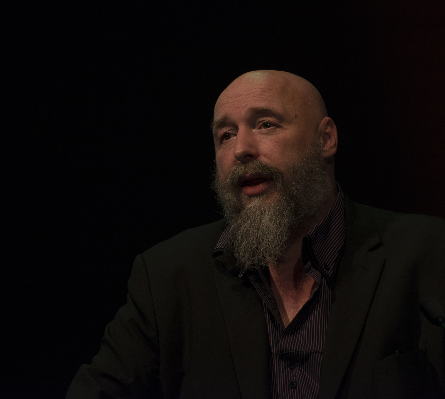man with beard in black suit sitting on stage