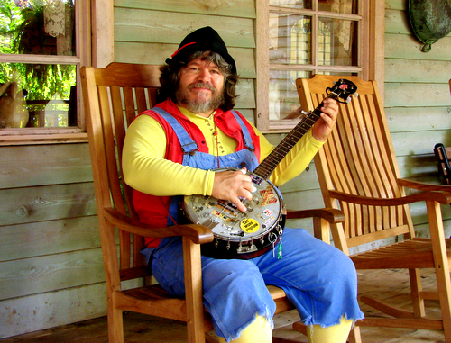 a man wearing yellow and blue is sitting in a rocking chair with an guitar