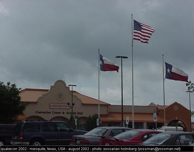 several flags flying high over an airport parking lot