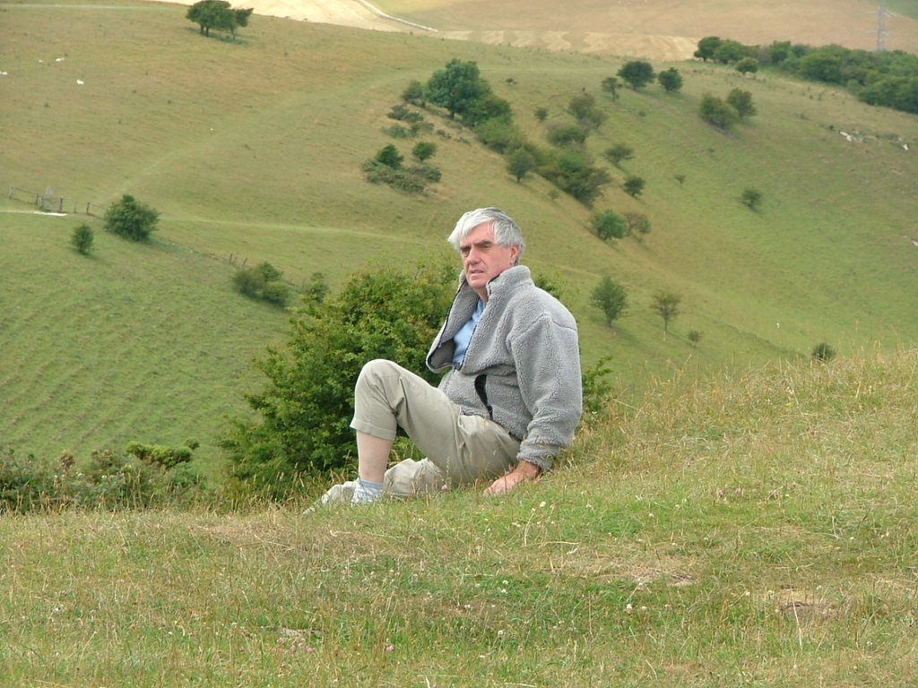 a man sitting in the grass on top of a hill