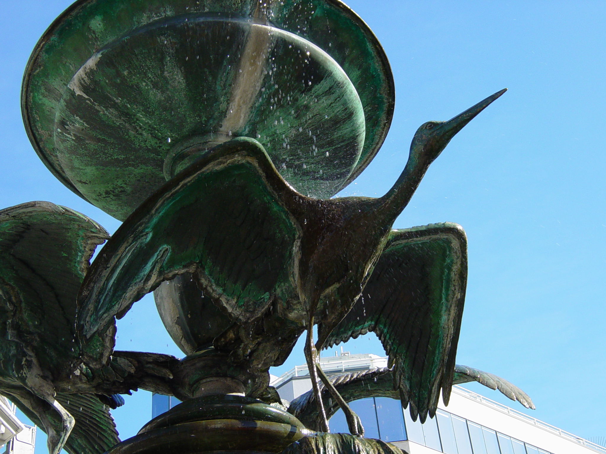 a green sculpture of two birds near a building