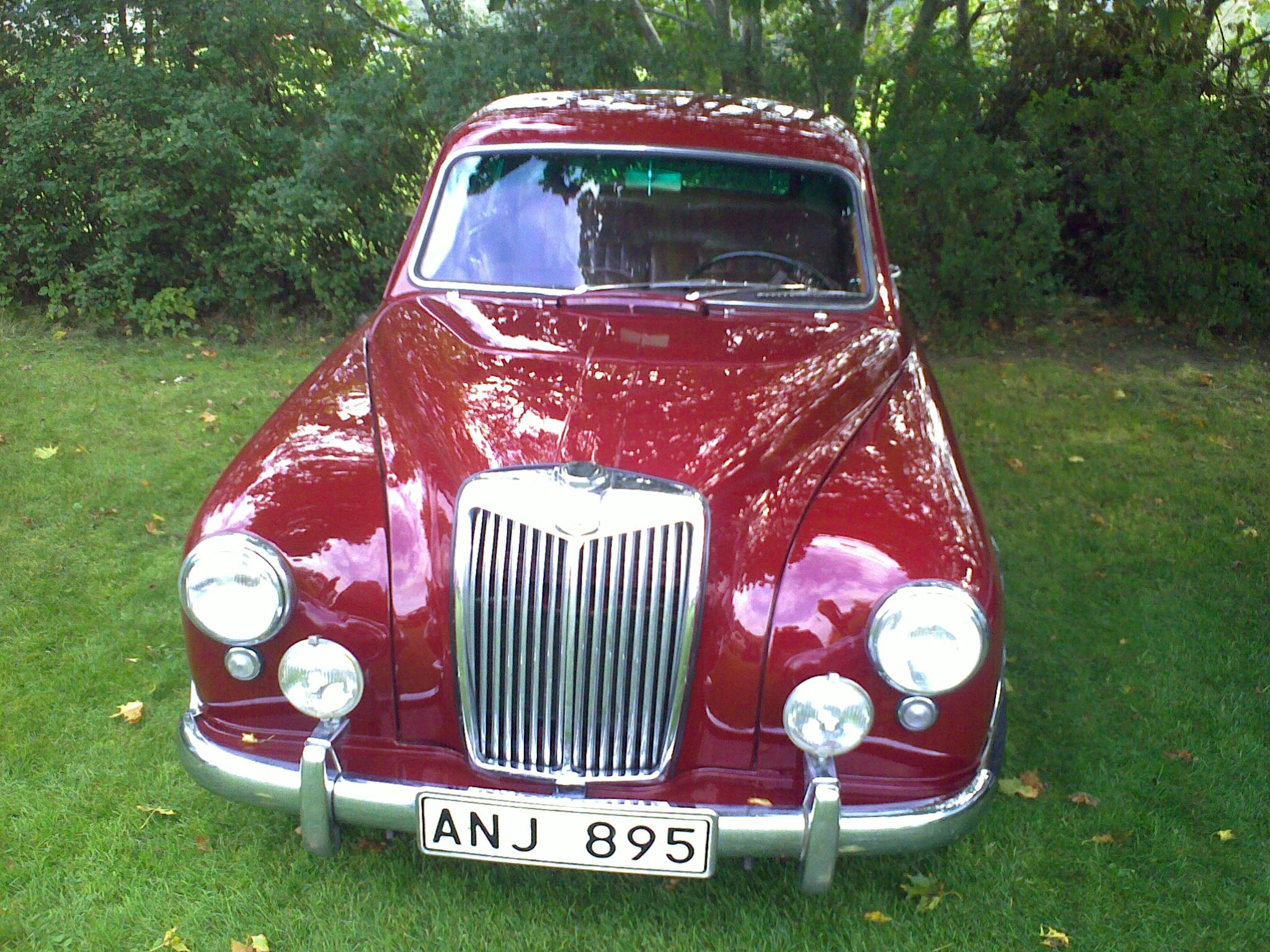 an antique red car sitting in the middle of the grass