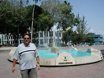 man in sunglasses stands next to fountain on a park