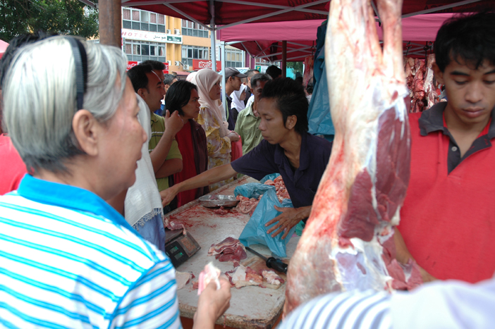 many people are in a market place looking at meat