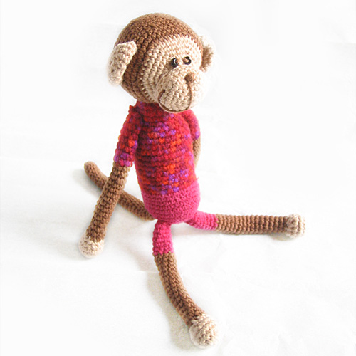 a knitted monkey wearing a red shirt sits on the ground