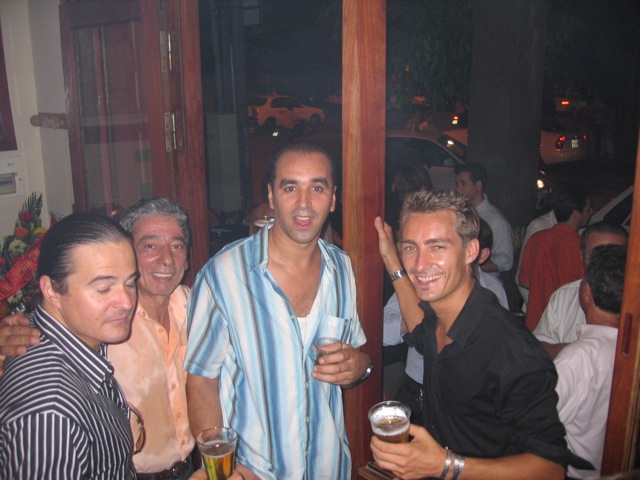 several men posing for a picture while one is drinking
