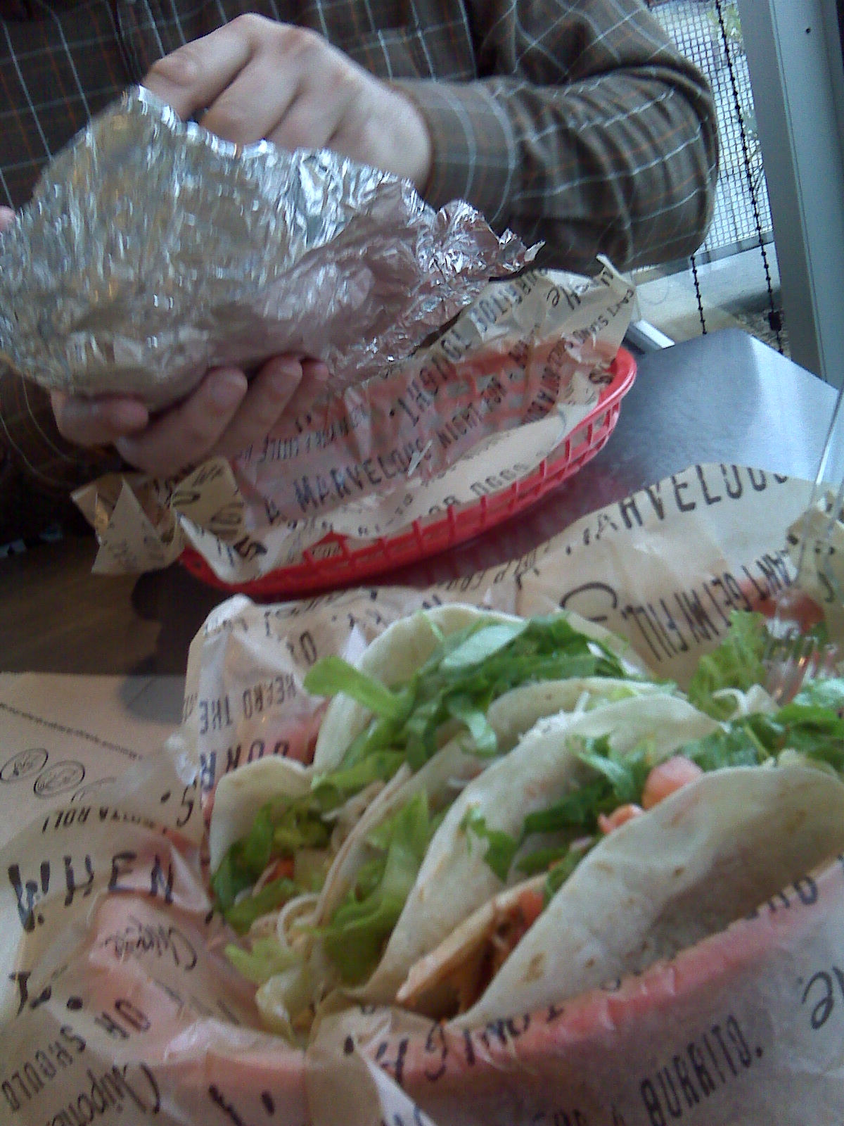 two people are holding sandwiches in plastic wrap