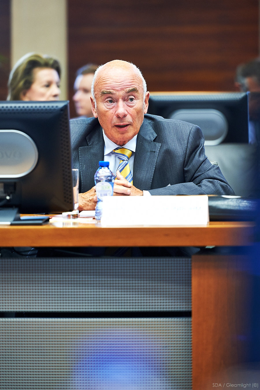 a man wearing a suit and tie sits at a desk with his laptop computer in front of him