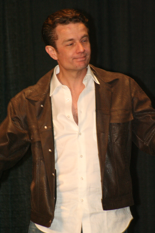 a man wearing a jacket talking in front of a microphone