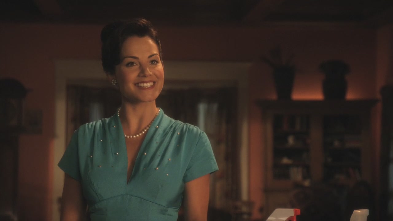 a woman wearing pearls standing in a kitchen