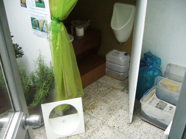a toilet next to a window, near some garbage and containers