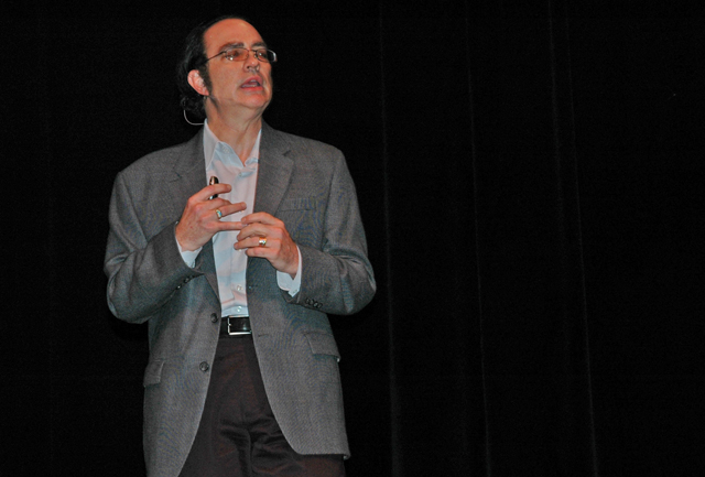 a man in glasses on stage with his hands folded