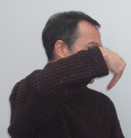 a man wearing glasses and a brown sweater covering his mouth