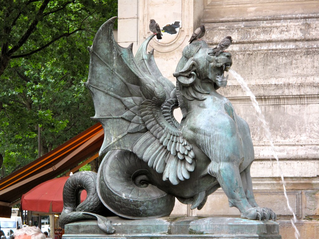 a large, winged statue near a building and water fountain