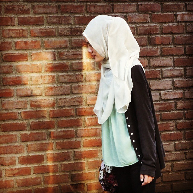 a girl wearing a hijab is standing next to a brick wall