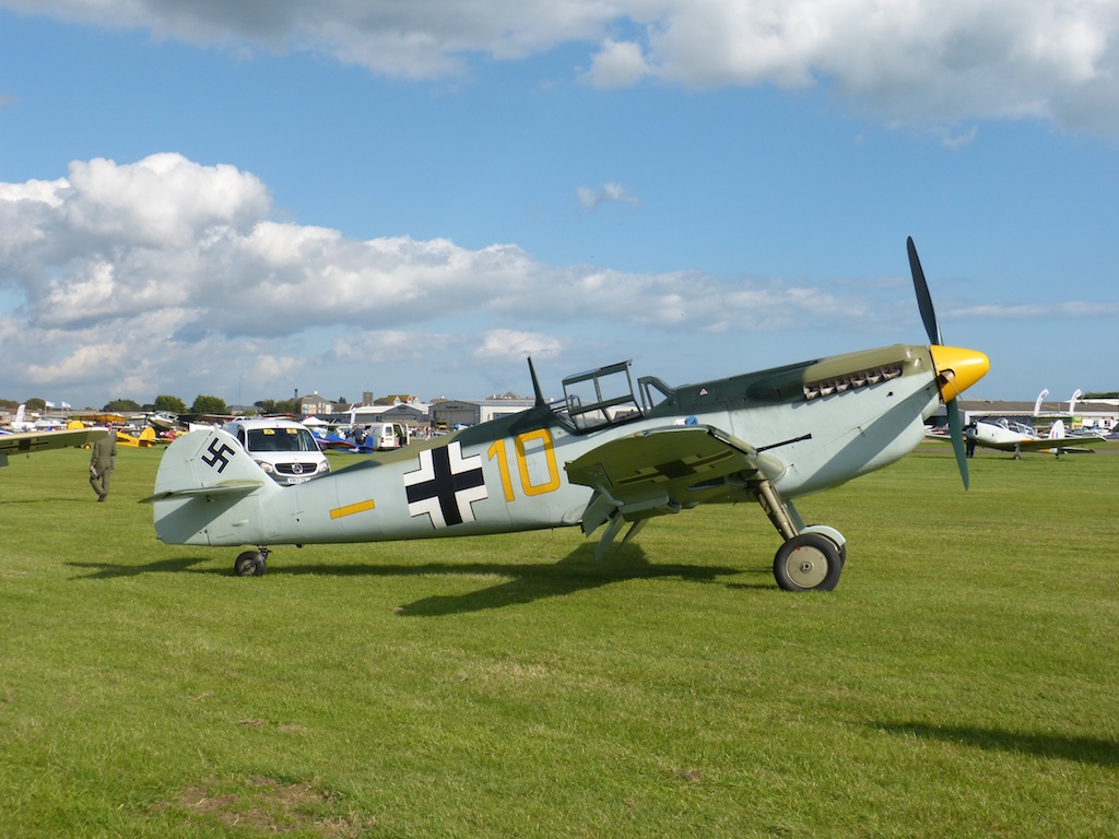 people standing near an old fashioned plane parked on the grass