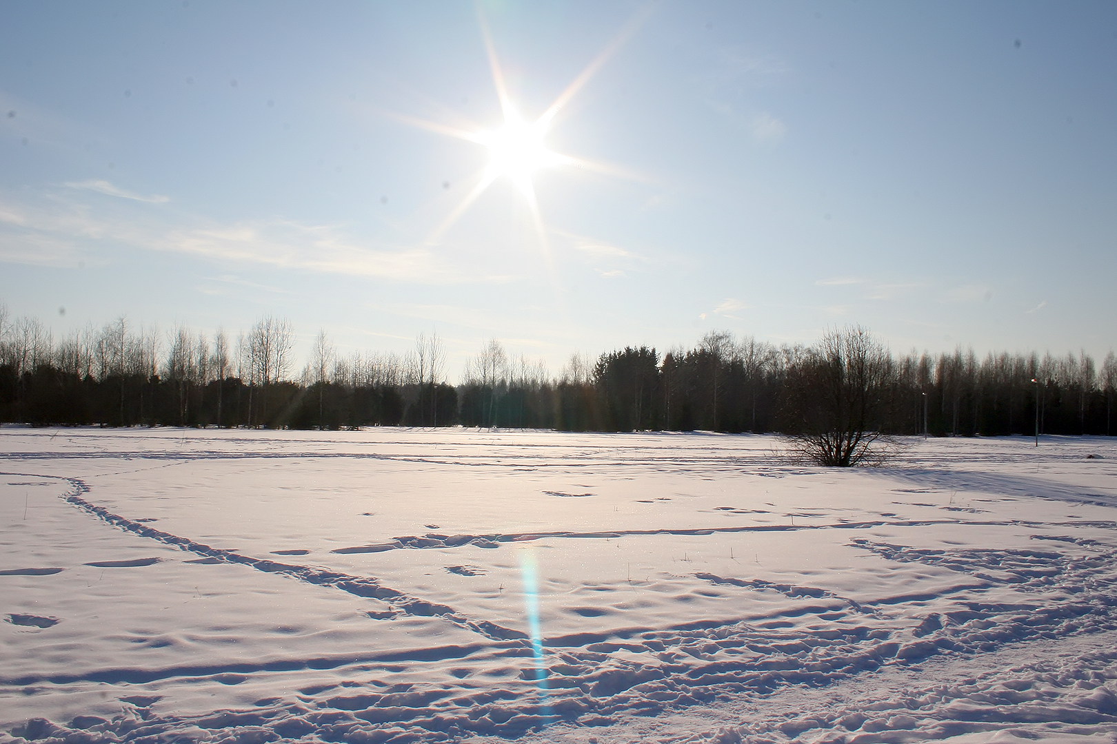 a field covered in snow with the sun shining above it