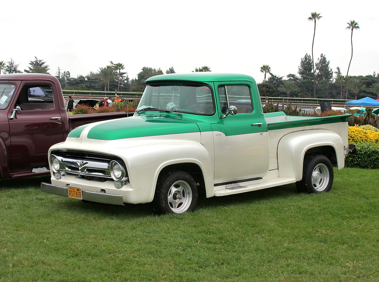 an older truck is parked in the grass next to a red and white truck