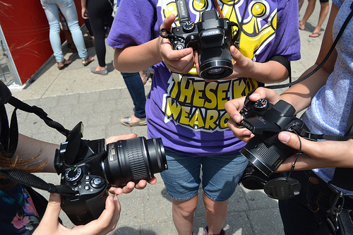 many people are surrounding a woman holding her camera and she is also using the phone