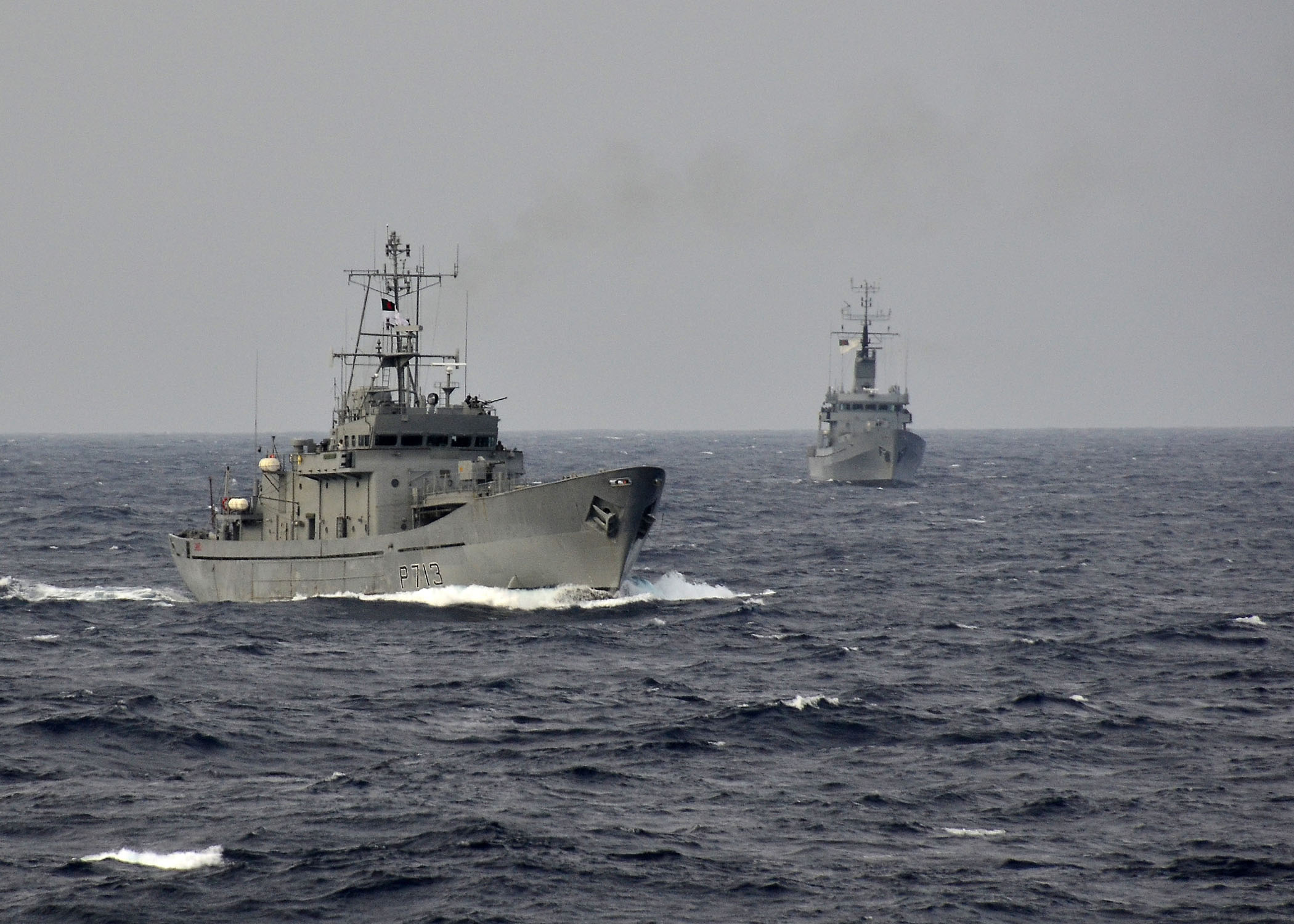 two ships travelling together in the ocean on a cloudy day