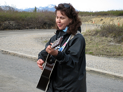 woman with guitar standing on roadway near mountains