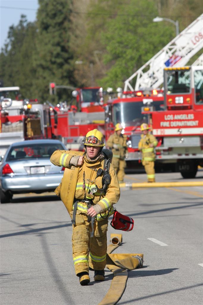 two fire fighters walking down the street by some cars