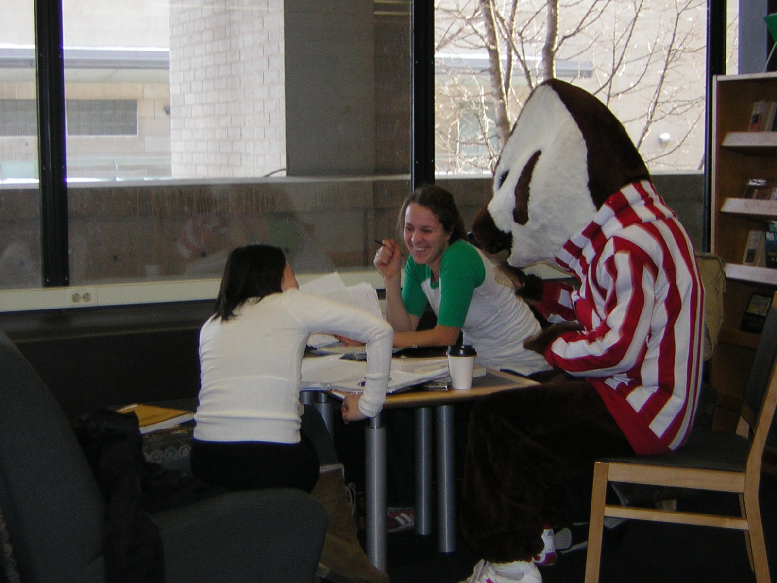 two women are seated at a desk with a mascot in front of them