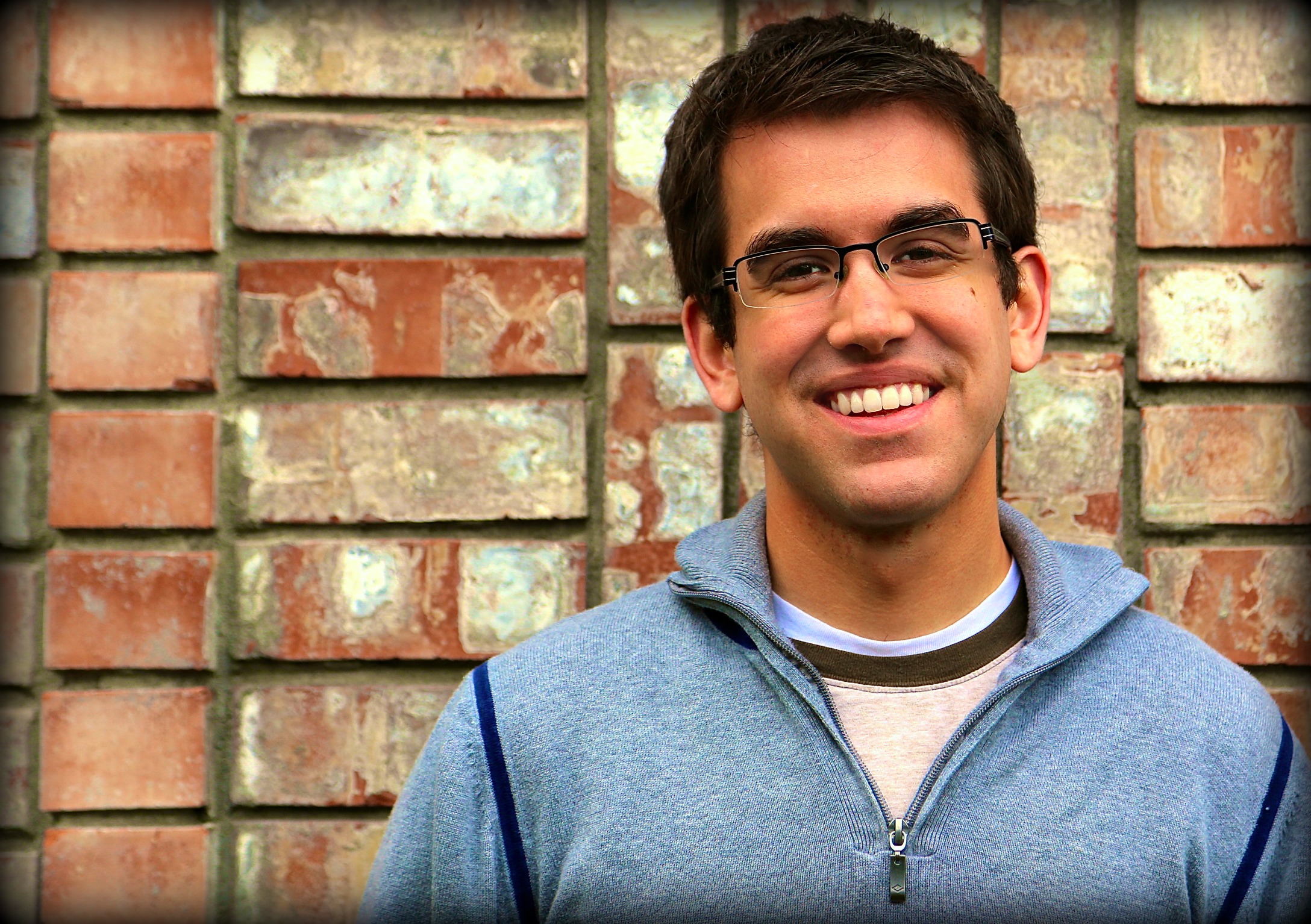 a man standing in front of a brick wall with glasses