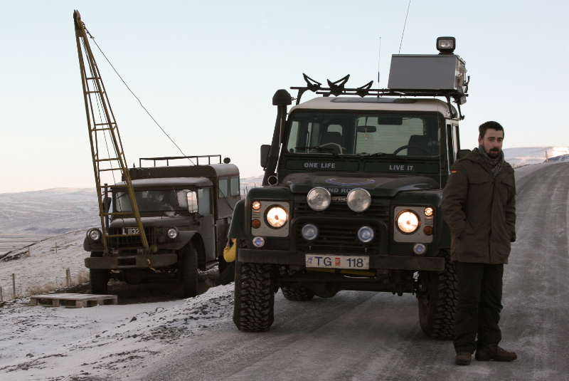 two men stand on the side of a road next to a utility vehicle