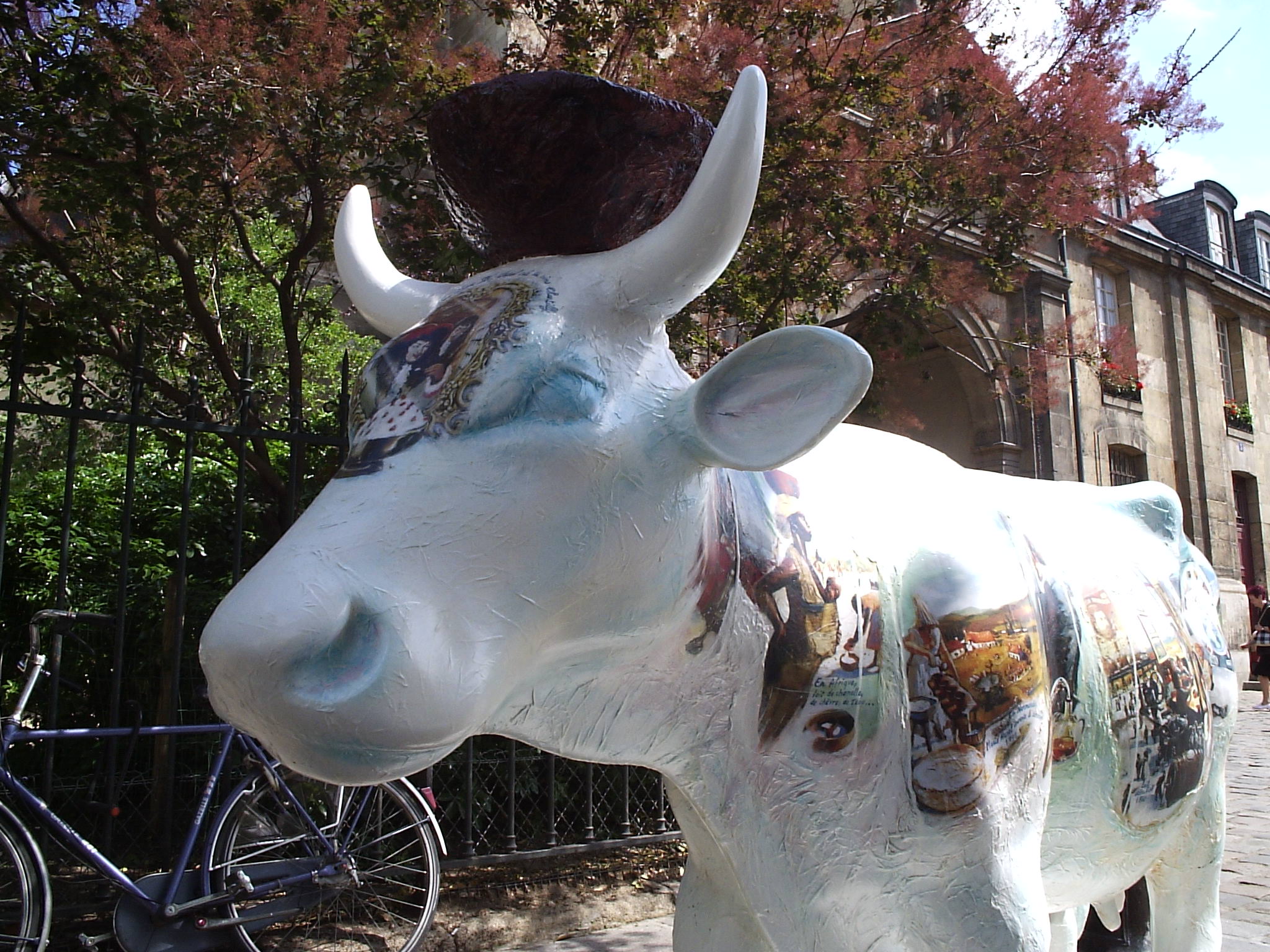 a large cow on a sidewalk with a bicycle in the background