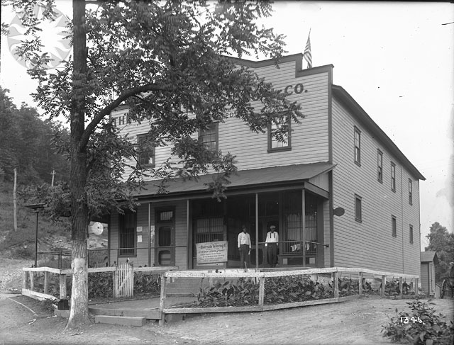 black and white pograph of two men standing on porch of large home
