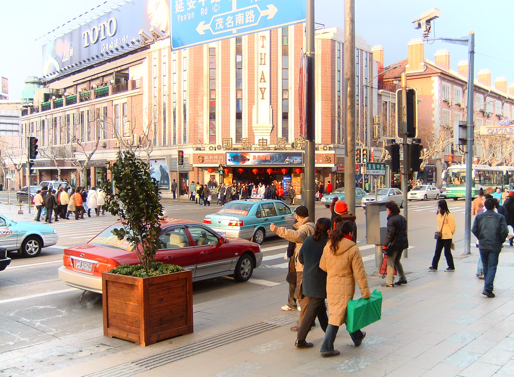 people walk and talk on the sidewalk near a busy street