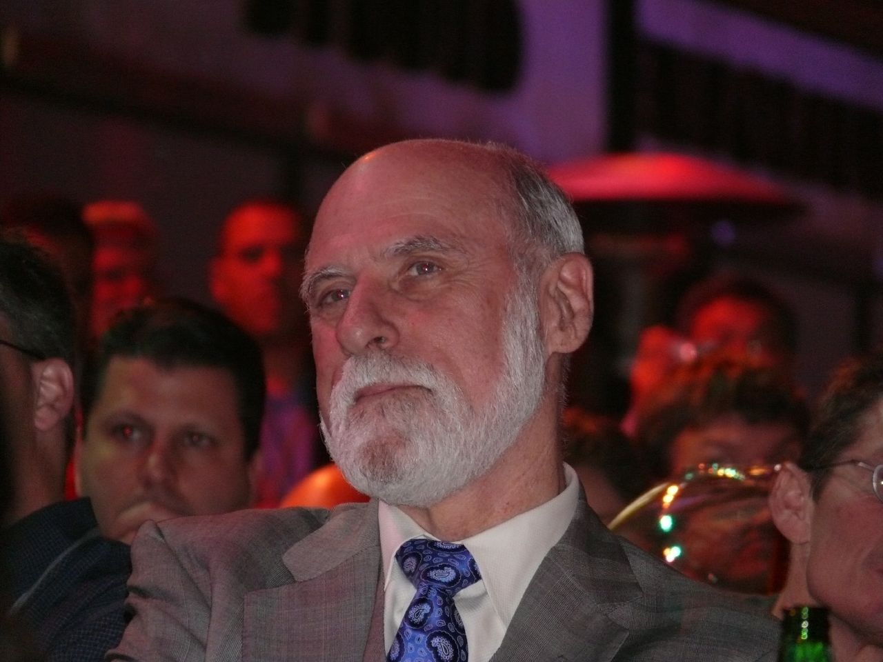 an older man in a suit sitting with people behind him