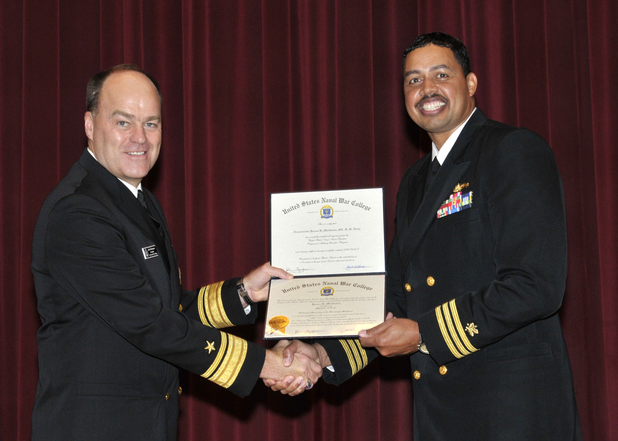 two men in uniform shaking hands over a certificate