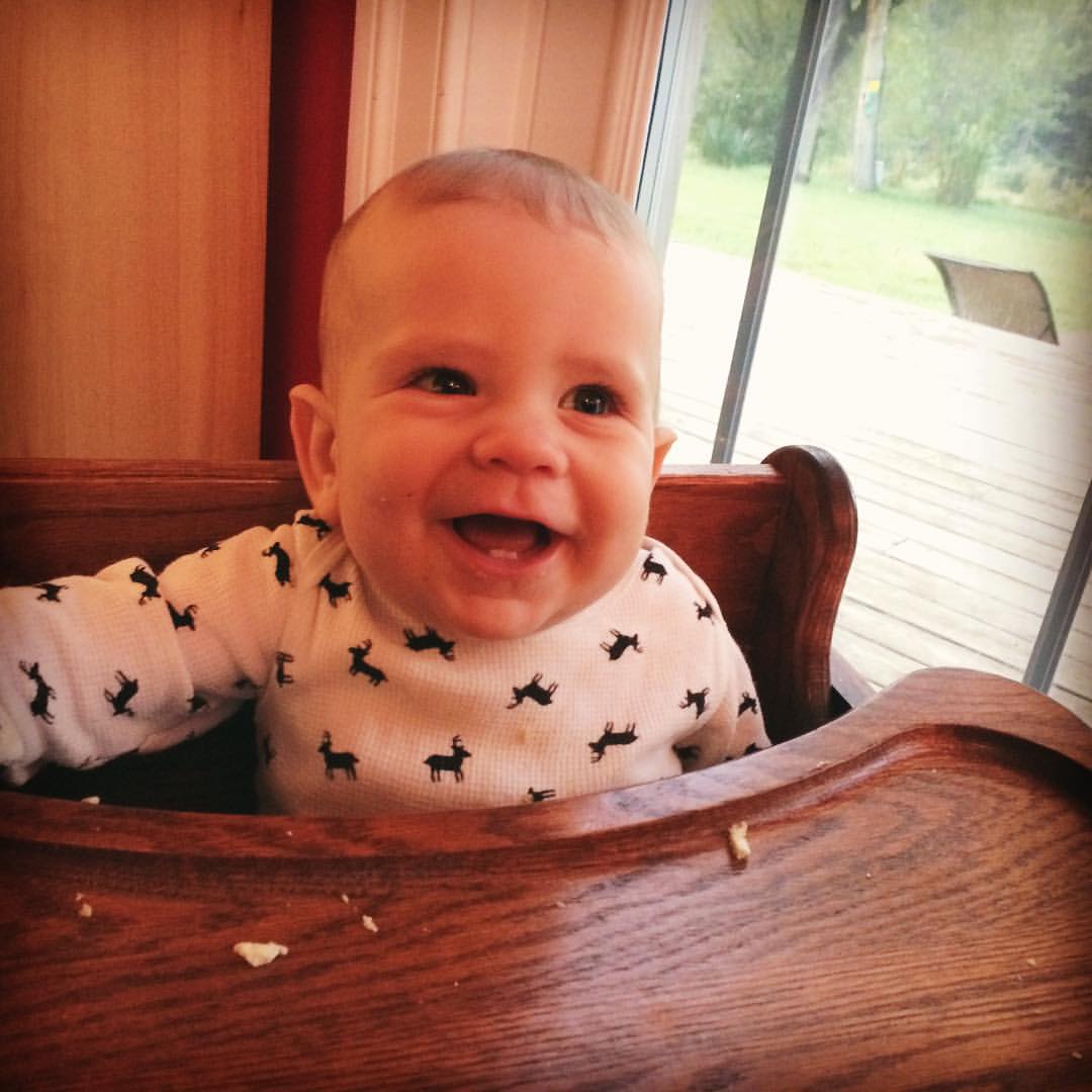 a baby sitting in a wooden high chair with his mouth open