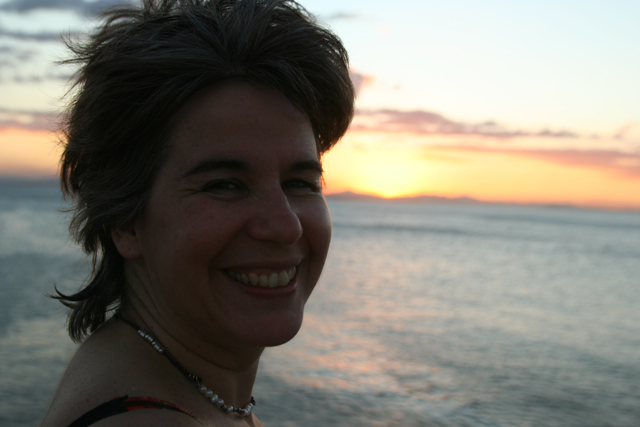 the woman is smiling near the water during sunset