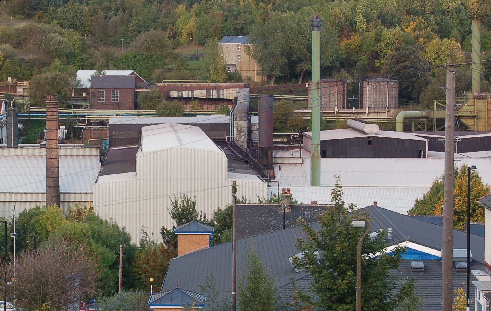 a factory with large pipes near to trees and houses