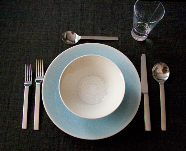 there is a white and blue plate with spoons and silverware