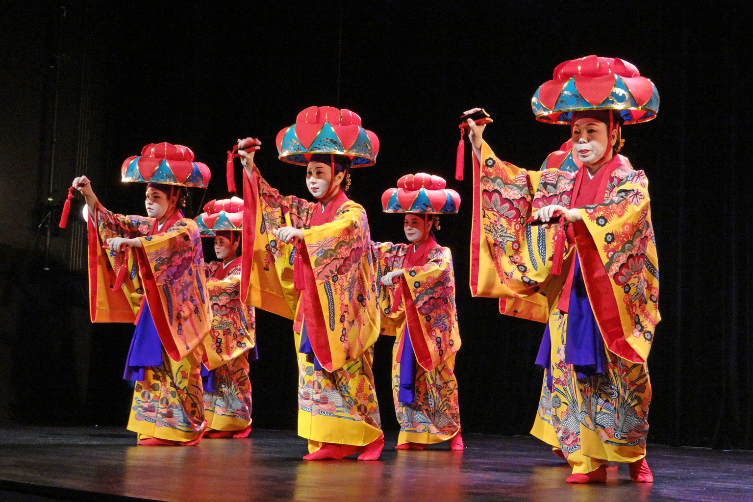 four japanese women in colorful traditional costume hold hands high above their heads