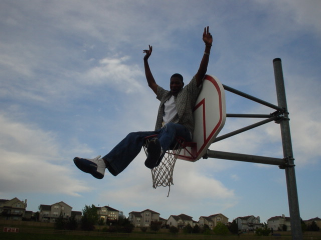 a man sits on a basketball hoop and poses for the camera