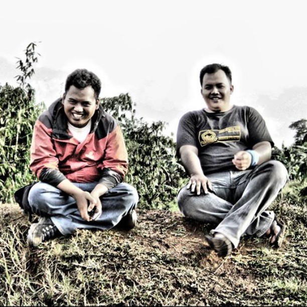 two men sitting on the grass while smiling at the camera