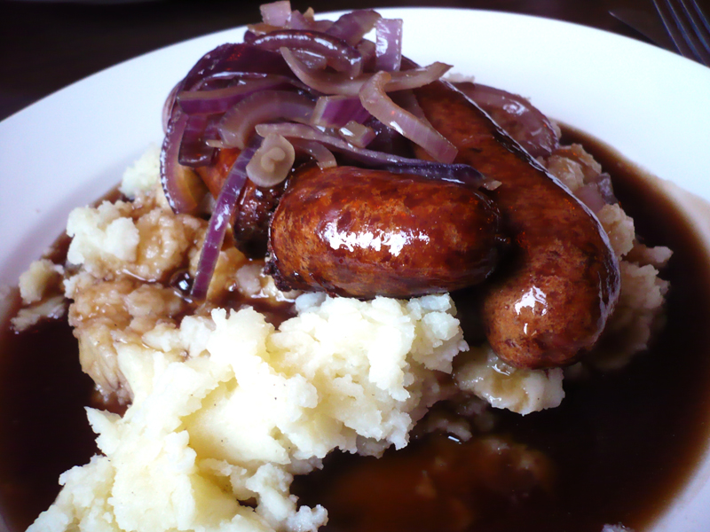 sausage and potatoes in gravy, sitting on a plate