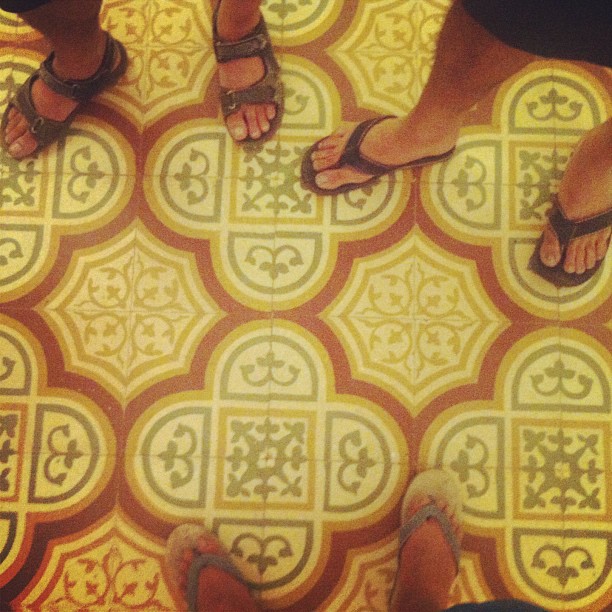 two pairs of feet with sandals on top of an area with intricate tiles