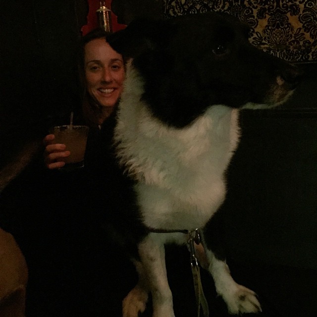 a woman is holding a drink with a dog on a leash