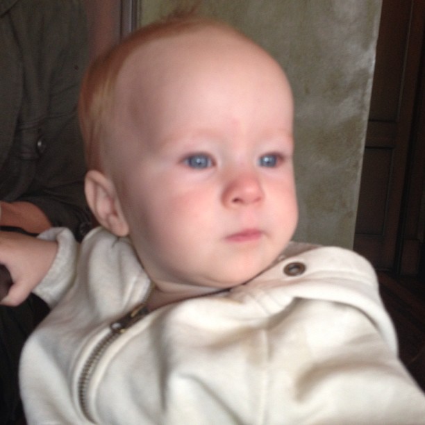 a bald baby with blue eyes wearing a white jacket
