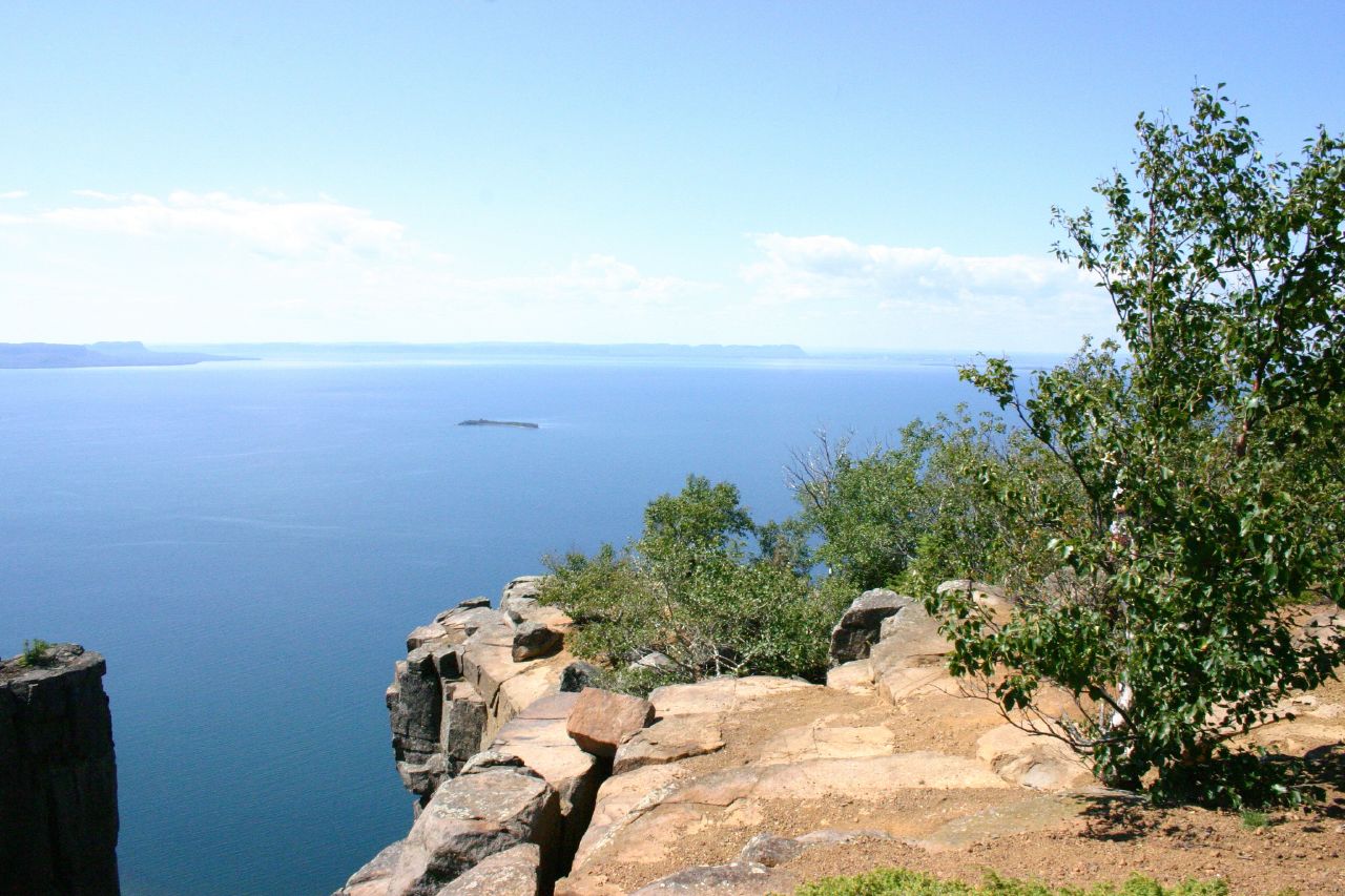 a blue sea and rocky cliff with trees