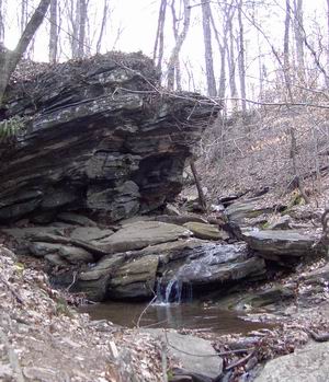 a small waterfall is running between a large rock cliff