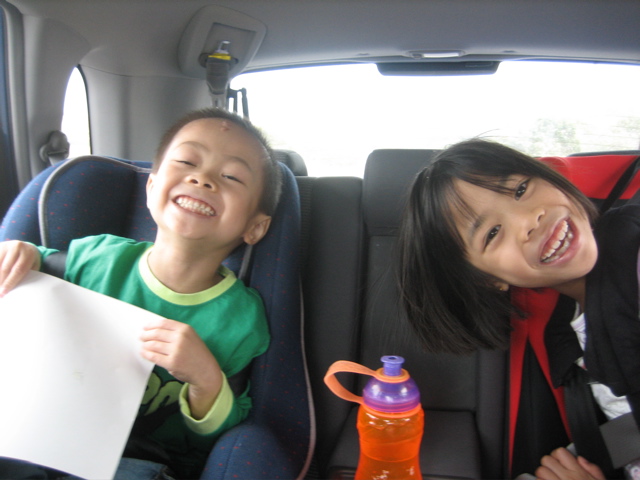 two children smiling and sitting in a car