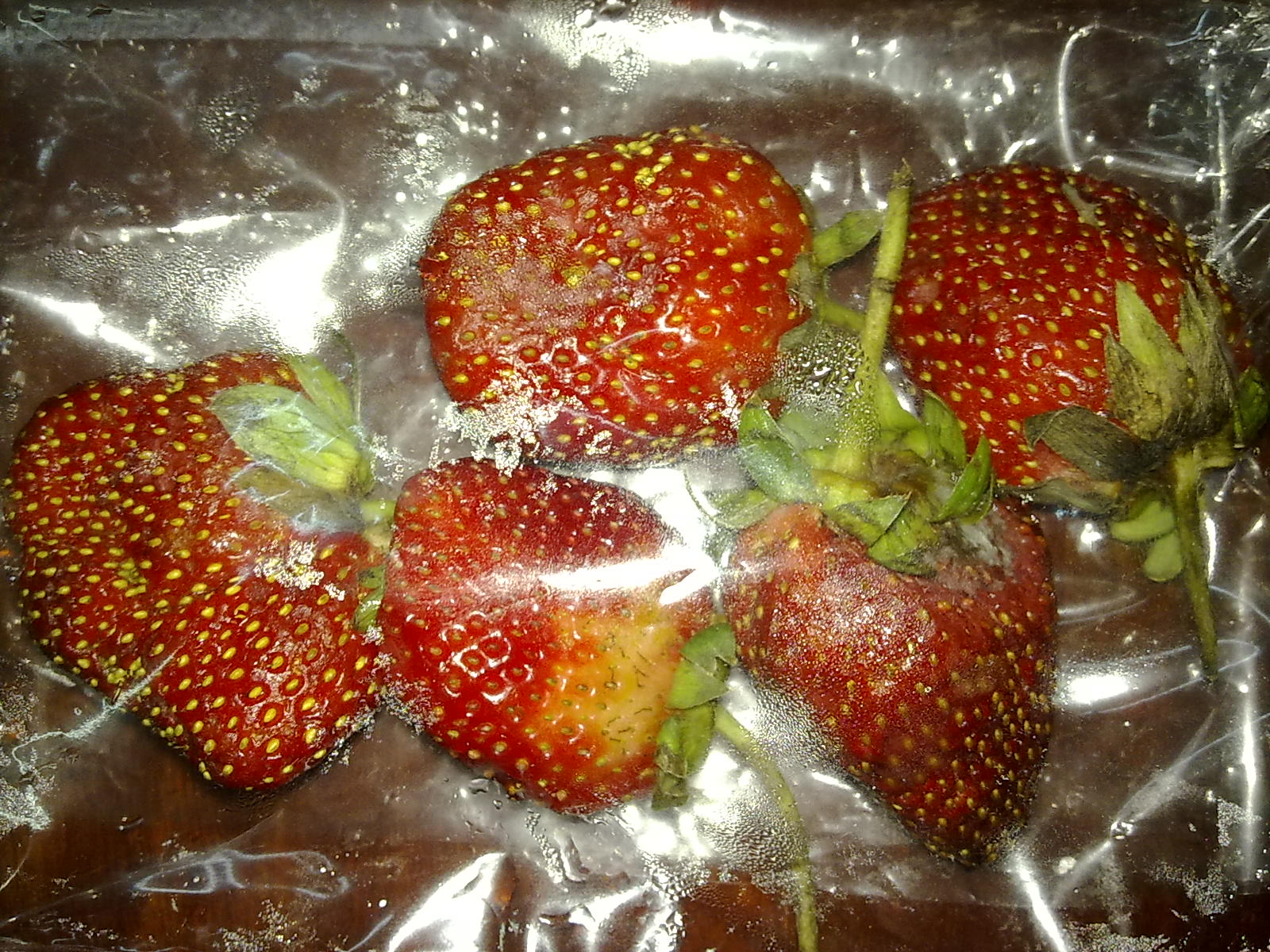 several strawberries sitting on plastic wrapped in plastic