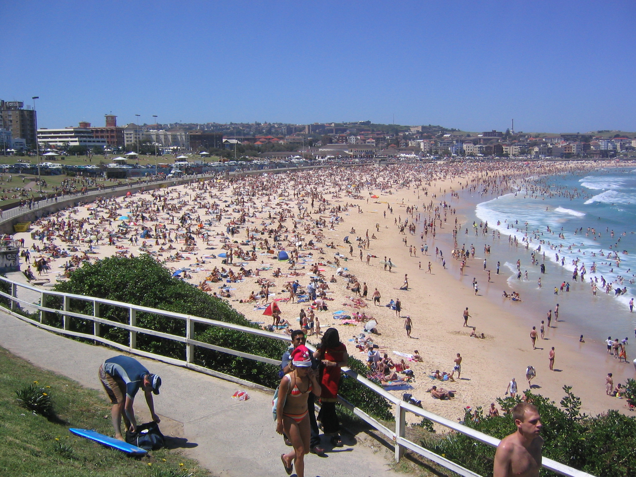 people walk on the path at the beach while they watch swimmers